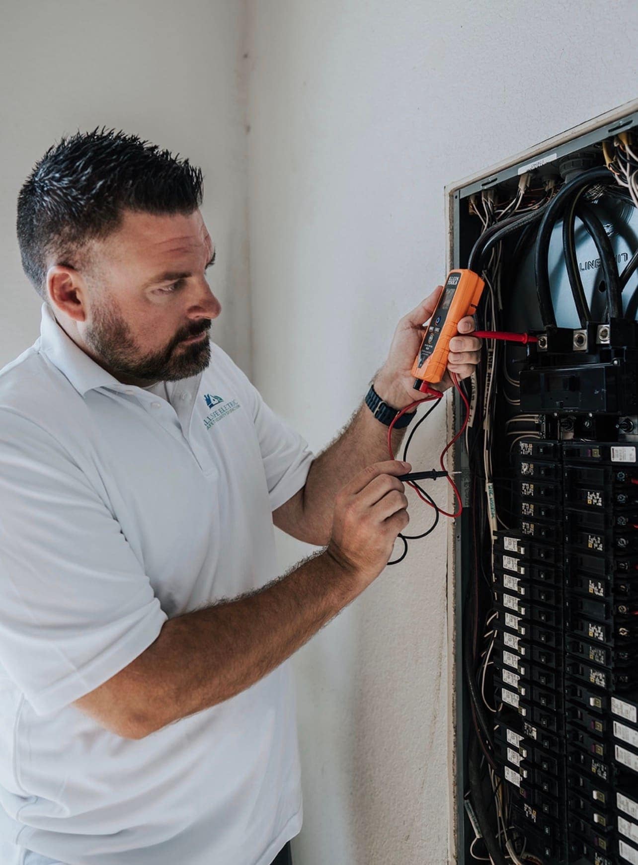 An Allsafe Electric electrician checking voltage at an open breaker panel