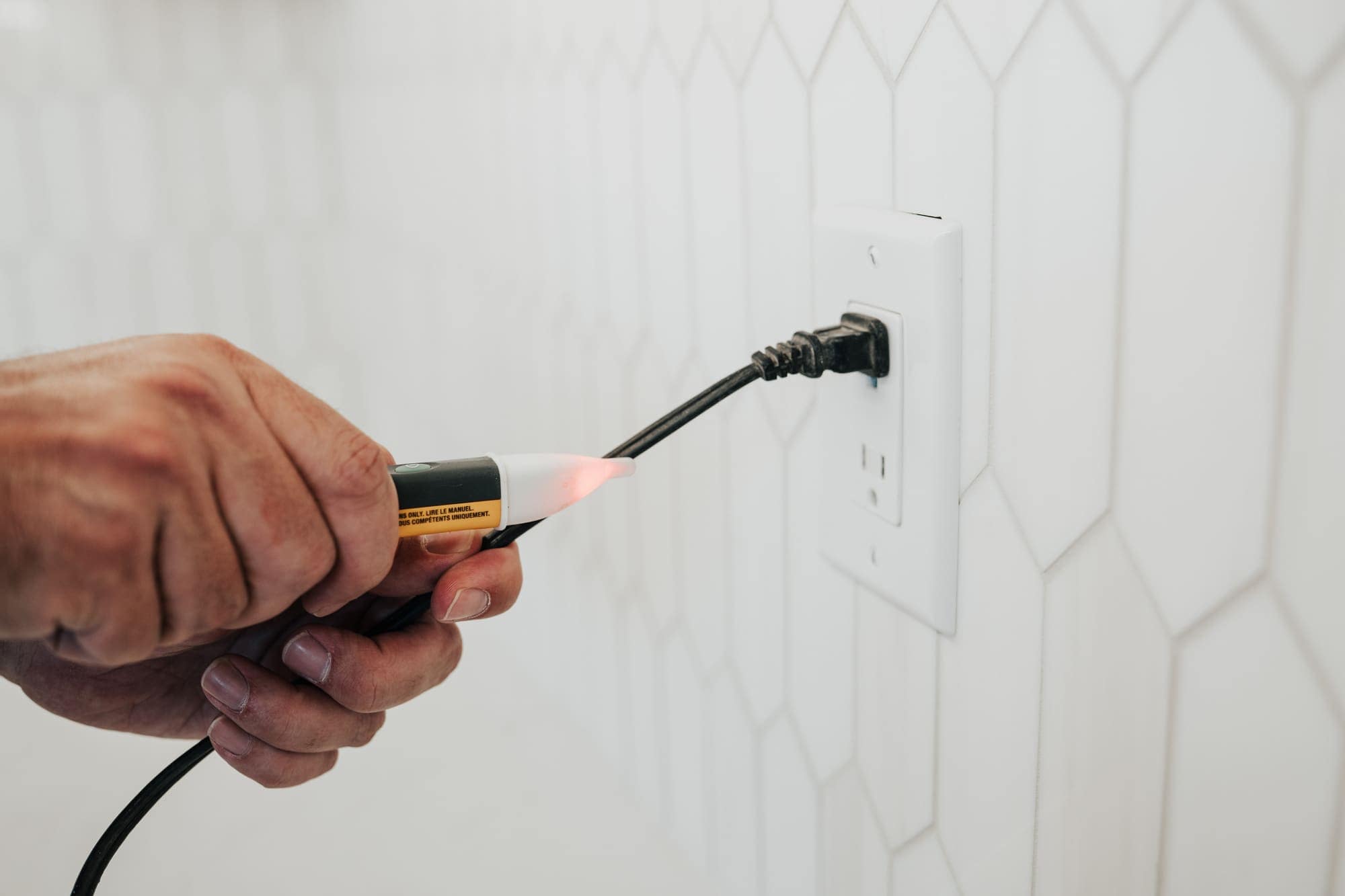 An Allsafe Electric electrician testing a kitchen outlet with a voltage detector